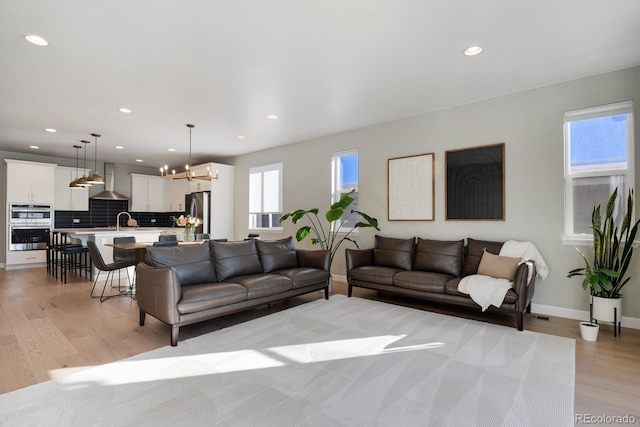 living room featuring an inviting chandelier, sink, and light hardwood / wood-style flooring