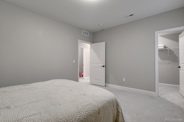 bedroom featuring a walk in closet, a closet, and light carpet