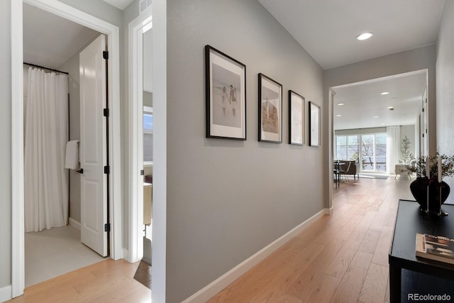 hall featuring baseboards, recessed lighting, and light wood-style flooring