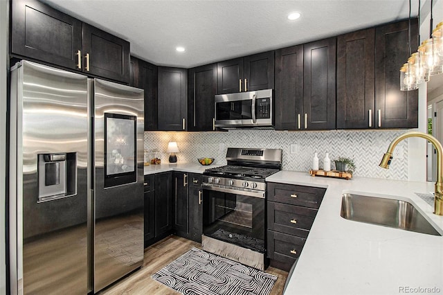 6775 Newland St, Arvada, CO 80003 - kitchen with appliances with stainless steel finishes, a sink, light wood-style floors, backsplash, and hanging light fixtures