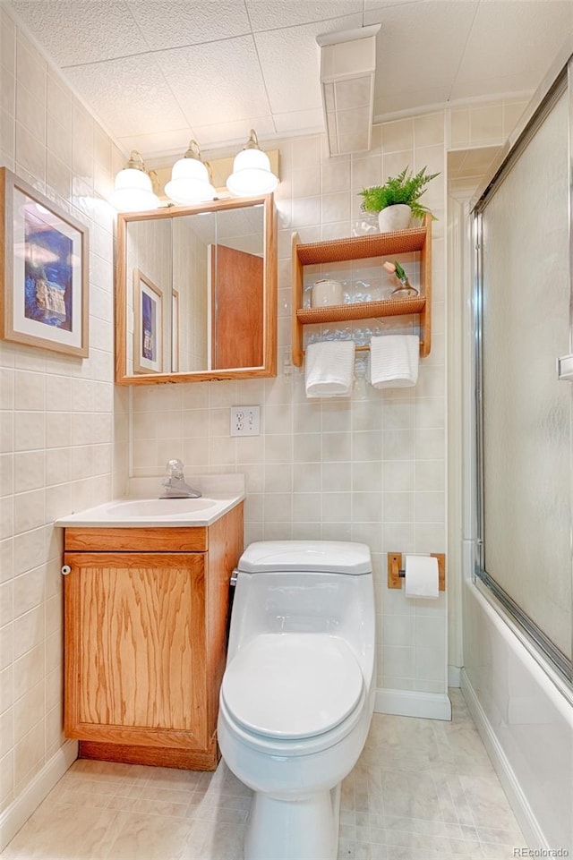 9100 Yucca Way, Thornton, CO 80229 - bathroom with tile walls, toilet, bath / shower combo with glass door, and vanity