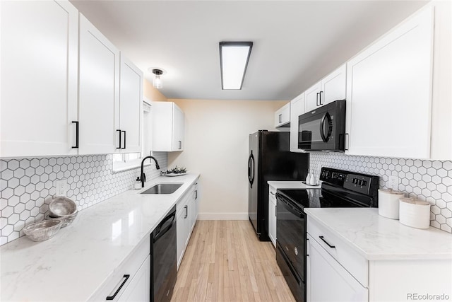 kitchen featuring black appliances, light stone counters, a sink, and white cabinetry