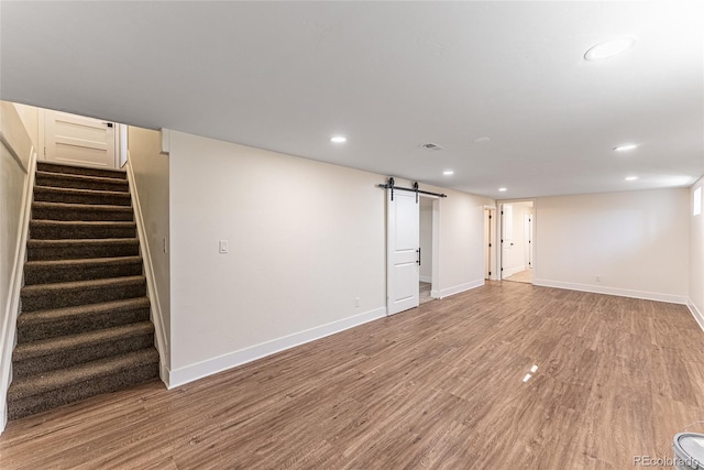 finished basement with a barn door, recessed lighting, wood finished floors, baseboards, and stairway