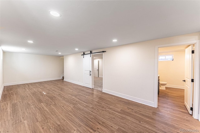 below grade area featuring baseboards, a barn door, wood finished floors, and recessed lighting