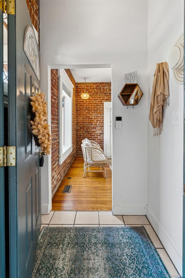 interior space with baseboards, visible vents, brick wall, and light tile patterned floors