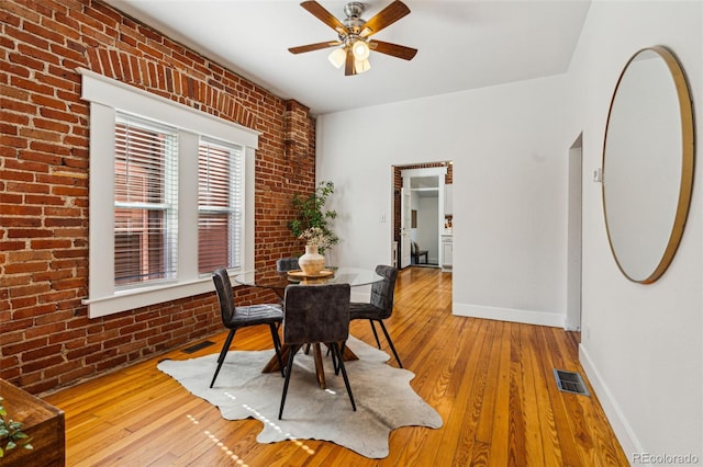 dining area with baseboards, visible vents, brick wall, and hardwood / wood-style flooring