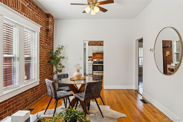 dining room with visible vents, baseboards, a ceiling fan, brick wall, and light wood-style flooring