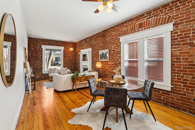 dining area featuring hardwood / wood-style flooring, brick wall, a fireplace, and baseboards