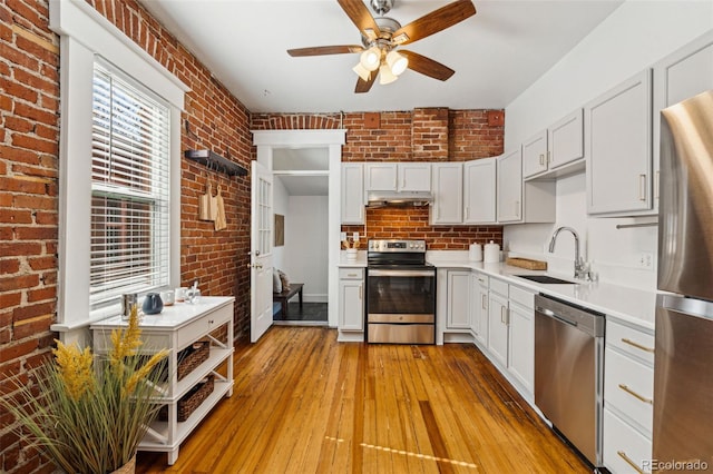 kitchen with under cabinet range hood, brick wall, stainless steel appliances, a sink, and light countertops