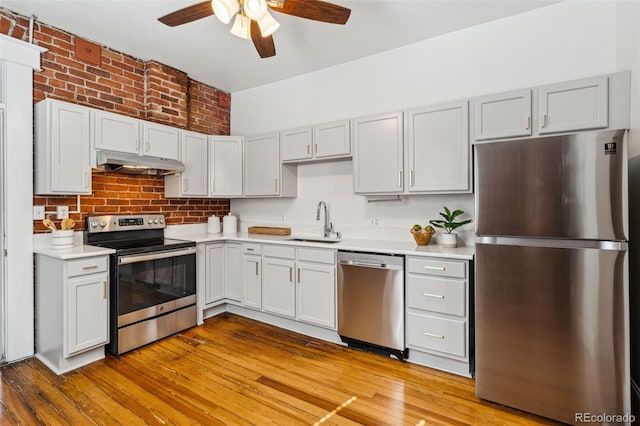 kitchen with under cabinet range hood, a sink, light countertops, appliances with stainless steel finishes, and light wood finished floors