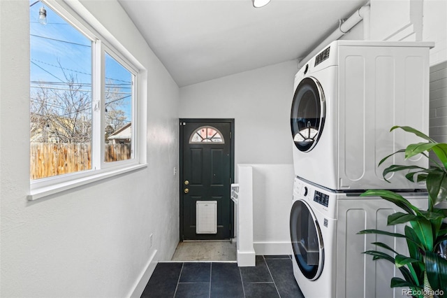 laundry room with laundry area, baseboards, stacked washer / drying machine, and dark tile patterned flooring