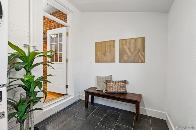 entryway featuring dark tile patterned floors, brick wall, and baseboards