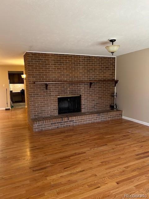 unfurnished living room featuring a brick fireplace, baseboards, and wood finished floors