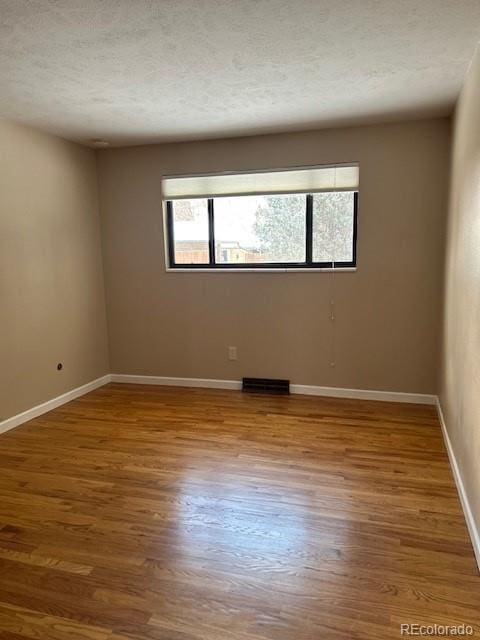 empty room with a textured ceiling, wood finished floors, and baseboards