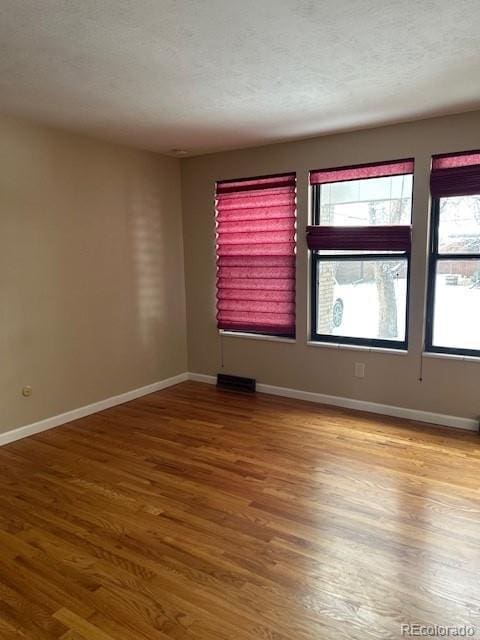 unfurnished room featuring a textured ceiling, baseboards, and wood finished floors