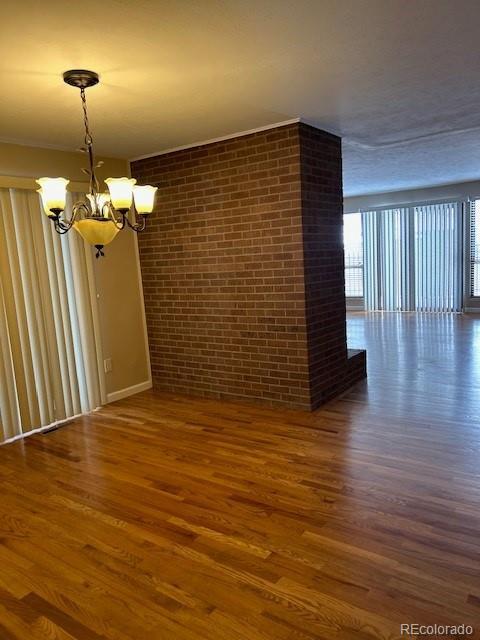 spare room with an inviting chandelier, brick wall, and dark wood finished floors