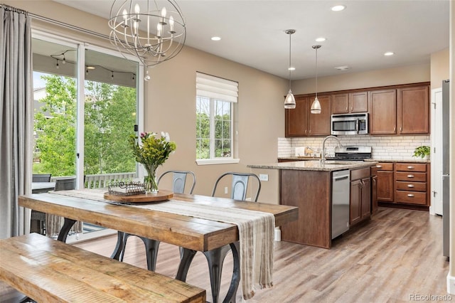 3319 Starry Night Loop, Castle Rock, CO 80109 - kitchen with stainless steel appliances, light wood finished floors, a chandelier, backsplash, and light stone counters