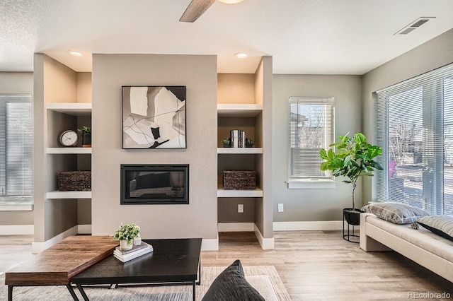 sitting room with built in shelves, light hardwood / wood-style flooring, and ceiling fan