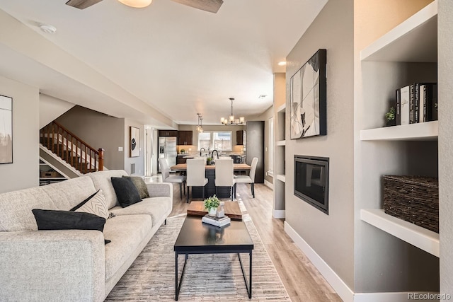 living room with built in shelves, light hardwood / wood-style flooring, and an inviting chandelier