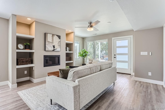 living room with ceiling fan, built in shelves, a textured ceiling, and hardwood / wood-style floors