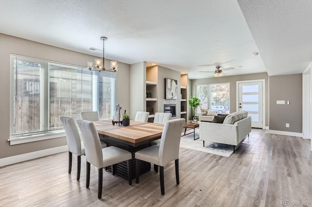 dining room with ceiling fan with notable chandelier, a wealth of natural light, light hardwood / wood-style flooring, and a textured ceiling