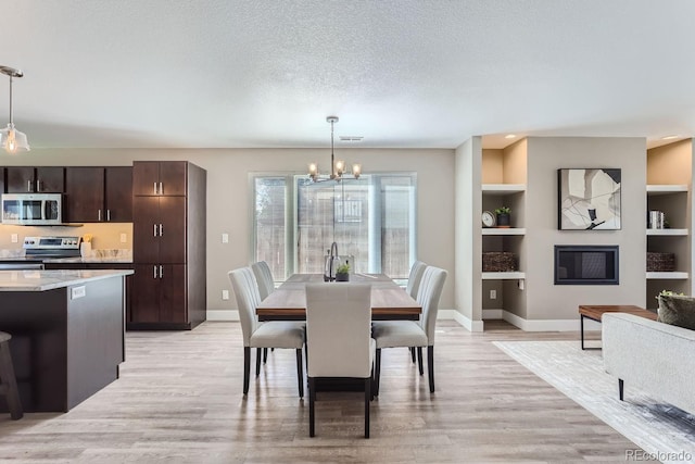 dining space featuring a textured ceiling, built in features, a chandelier, and light hardwood / wood-style flooring