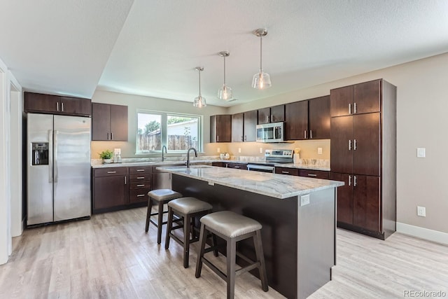 kitchen featuring stainless steel appliances, dark brown cabinetry, a center island with sink, and decorative light fixtures