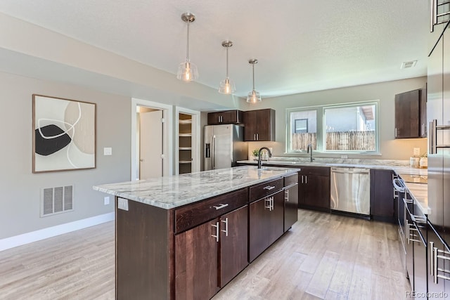 kitchen with an island with sink, pendant lighting, dark brown cabinetry, and stainless steel appliances