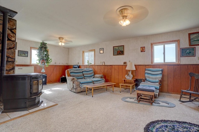 carpeted living room with a wood stove, wooden walls, and ceiling fan