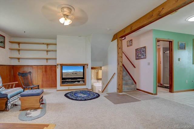 carpeted living room featuring beamed ceiling, wooden walls, and ceiling fan