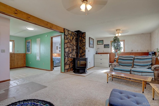 carpeted living room with a wood stove, beamed ceiling, plenty of natural light, and ceiling fan