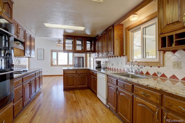 kitchen with dishwasher, light stone counters, light wood-type flooring, sink, and oven