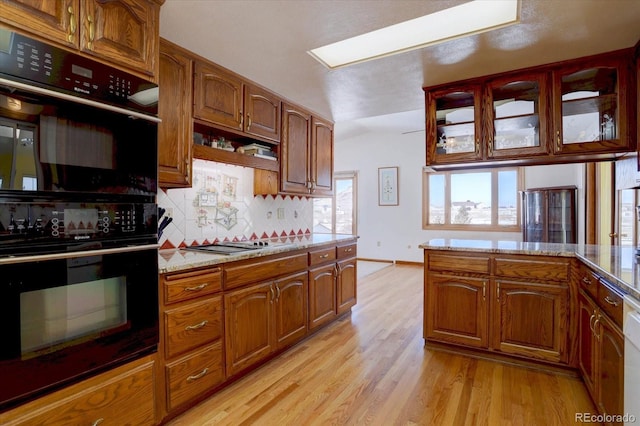 kitchen with backsplash, black appliances, light stone countertops, and light hardwood / wood-style flooring