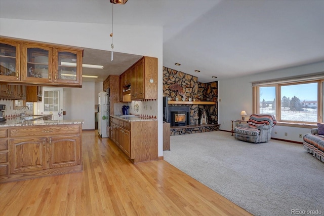 kitchen featuring lofted ceiling, light hardwood / wood-style flooring, sink, light stone counters, and a fireplace