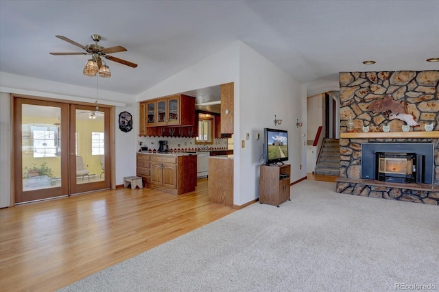 living room with french doors, ceiling fan, vaulted ceiling, a wood stove, and light colored carpet