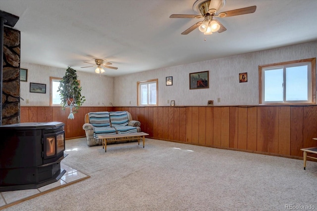 living area featuring ceiling fan, a wood stove, and light colored carpet