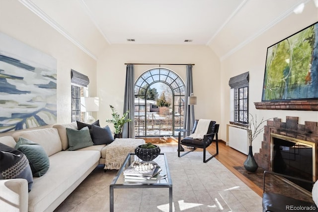 living room with a brick fireplace, crown molding, vaulted ceiling, and hardwood / wood-style flooring