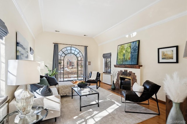 living room with a brick fireplace, vaulted ceiling, ornamental molding, and light wood-type flooring