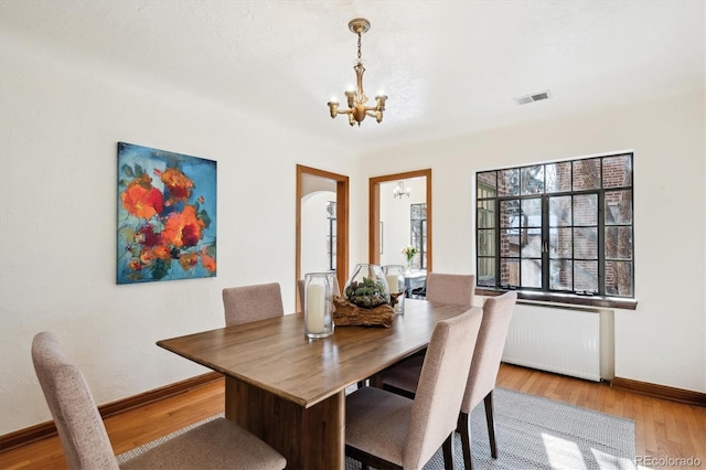 dining space featuring radiator heating unit, light wood-type flooring, and a notable chandelier