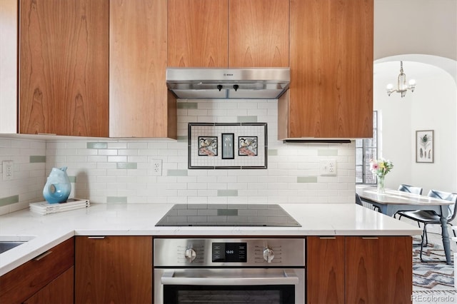 kitchen with black electric stovetop, backsplash, light stone countertops, and stainless steel oven