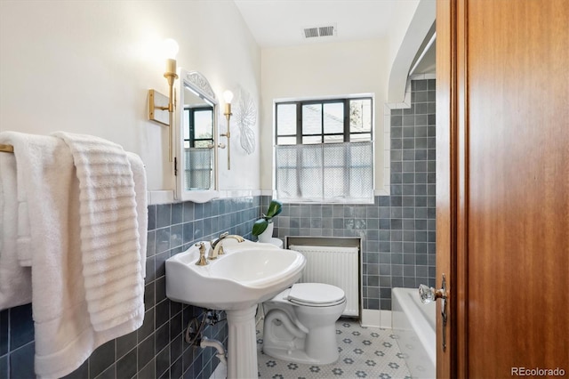 bathroom featuring toilet, tile walls, radiator heating unit, tile patterned flooring, and a washtub