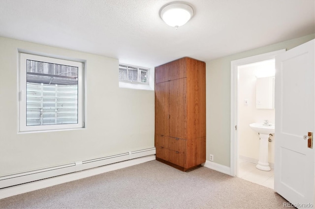 unfurnished bedroom featuring a baseboard radiator, ensuite bath, and light carpet