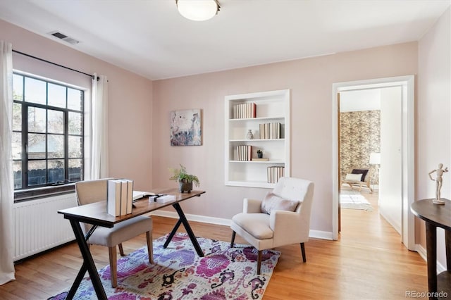 office featuring radiator, light wood-type flooring, and built in shelves