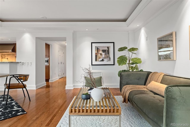 living room featuring wood finished floors, baseboards, recessed lighting, ornamental molding, and a raised ceiling