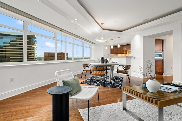 living room featuring a raised ceiling, light wood-type flooring, baseboards, and ornamental molding