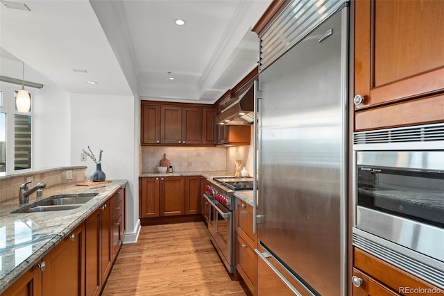 kitchen with custom exhaust hood, high quality appliances, sink, hanging light fixtures, and light stone countertops