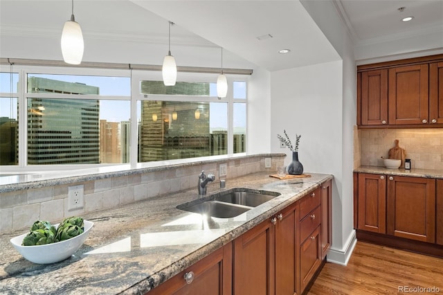 kitchen featuring crown molding, pendant lighting, wood finished floors, brown cabinetry, and a sink