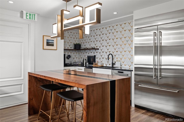 kitchen with a kitchen breakfast bar, sink, decorative backsplash, appliances with stainless steel finishes, and dark hardwood / wood-style flooring