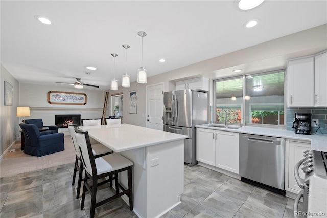 6504 W 85th Ave, Arvada, CO 80003 - kitchen with appliances with stainless steel finishes, a lit fireplace, white cabinets, a kitchen bar, and recessed lighting