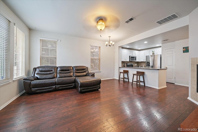 living room with a chandelier, a wealth of natural light, visible vents, and dark wood-type flooring